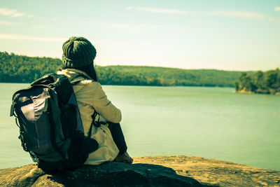 Rear view of man sitting on riverbank against sky