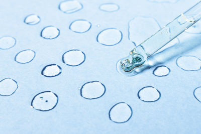 Cosmetic transparent drops on a blue background with a glass