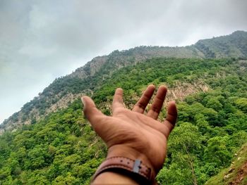 Cropped hand of man gesturing against mountain