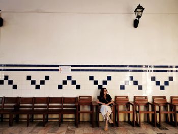 Woman sitting on bench against wall