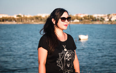 Portrait of young woman wearing sunglasses standing against sea