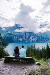 Rear view of people sitting by lake against sky