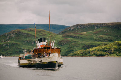 Ferry sailing on river against mountains