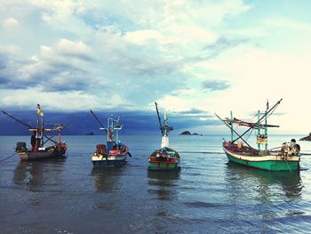 Boats in calm sea against cloudy sky