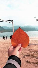 Midsection of person holding umbrella by sea against sky