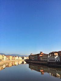 Reflection of buildings in canal against clear blue sky