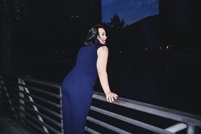 Portrait of young woman standing by railing at night