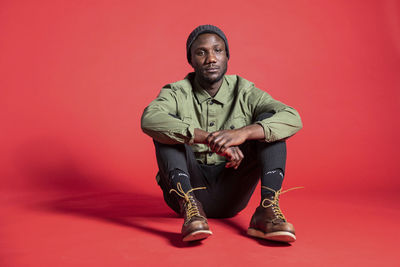 Portrait of young man sitting against red background