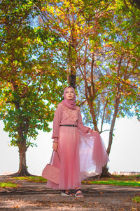 Portrait of woman standing by tree against plants