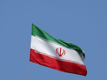 Low angle view of iranian flag against clear blue sky