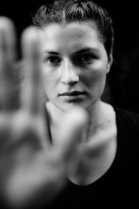 Portrait of serious young woman showing stop gesture against black background