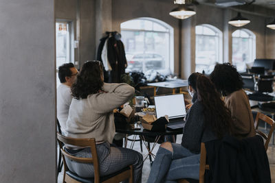 Young programmer working on laptop by male and female colleagues having lunch at startup company