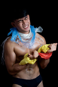 Shirtless young man holding plastic against black background