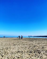 People on beach against clear blue sky