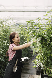 Female farmer holding digital tablet while working in greenhouse