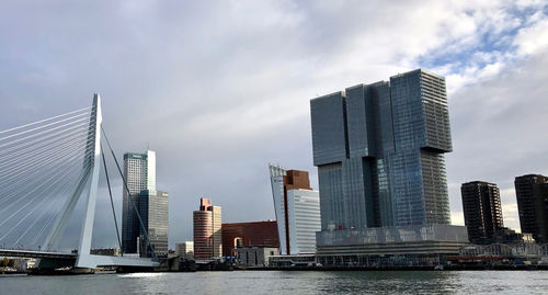 Modern buildings by river against clouded sky in city