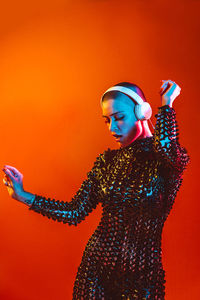 Young woman with shaved head wearing headphones against orange background