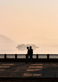 Silhouette men standing by railing against sky during sunset