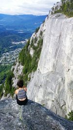 Rear view of woman sitting on cliff against sky