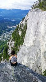 Rear view of woman looking at view while sitting on cliff