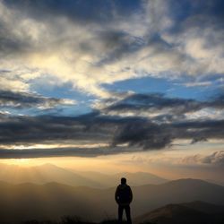 Rear view of silhouette hiker looking at mountains against sky during sunset