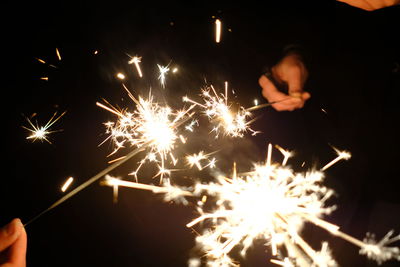 Cropped hands holding sparklers at night