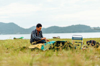 Young woman sitting on land against sky