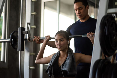 Young woman with fitness instructor lifting barbell at gym