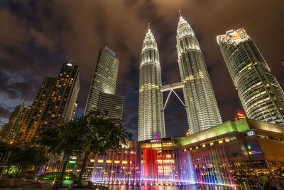 Low angle view of illuminated petronas towers amidst buildings at night