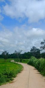 Empty road amidst field against sky