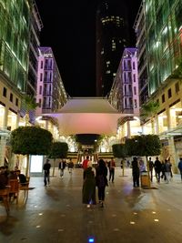 People on illuminated buildings in city at night