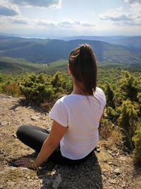 Rear view of woman sitting on landscape against mountain