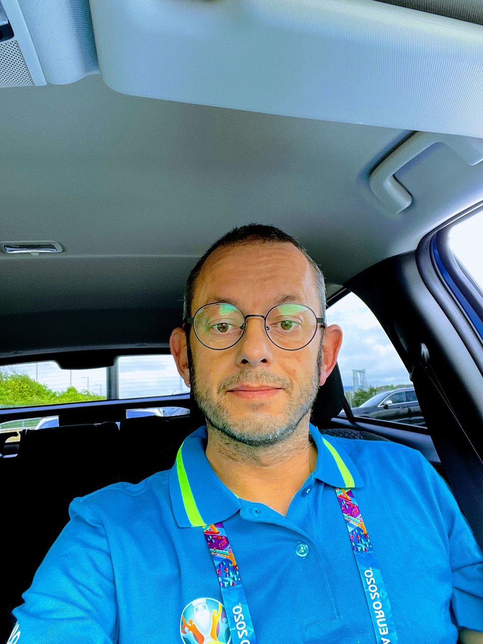 one person, adult, transportation, portrait, mode of transportation, men, motor vehicle, headshot, car, person, vehicle interior, mature adult, glasses, front view, looking at camera, eyeglasses, vehicle, travel, car interior, indoors, beard, facial hair, clothing, sitting, emotion, smiling, serious, driving, journey, seat belt, day