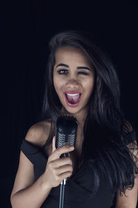 Portrait of young woman holding microphone against black background