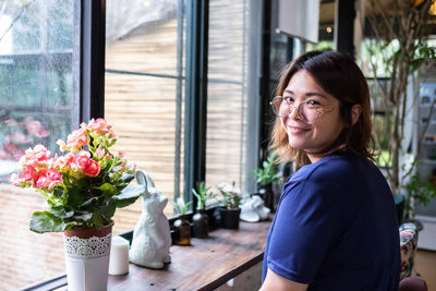 Portrait of smiling young woman standing by potted plant on table