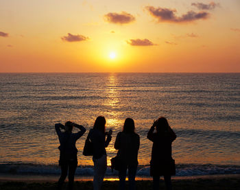 Silhouette people standing on beach during sunset