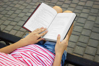 Midsection of woman reading book while sitting on street