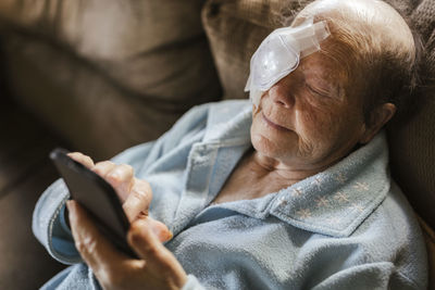 Injured senior woman using smart phone on sofa at home