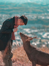 Side view of young man looking at deer while standing on field