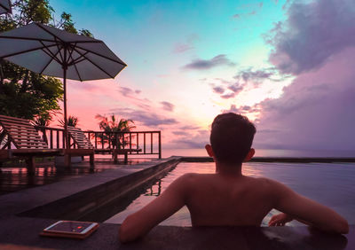 Rear view of shirtless boy in swimming pool against sky