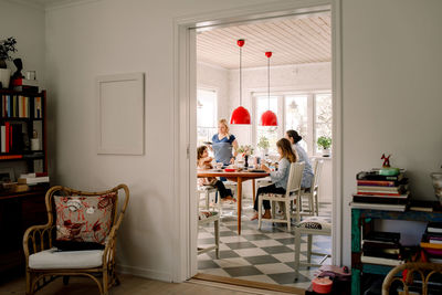 Mothers and daughters having breakfast at dining table seen through doorway