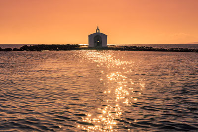 Building by sea against sky during sunset