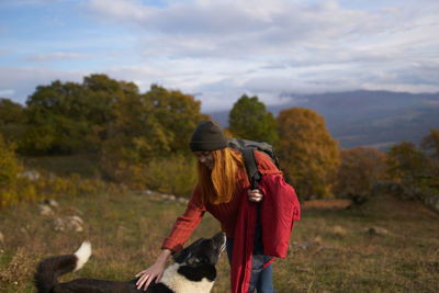 Rear view of woman with dog on field against sky
