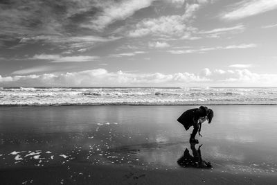 Woman bending on beach against sky