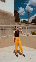 Full length of woman drinking water while standing against building in city