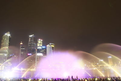 Illuminated modern buildings in city against sky at night