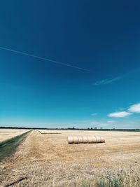 Hay bales on field against blue sky