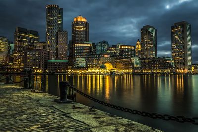 Illuminated buildings by river against sky at night