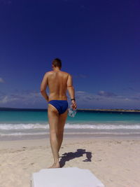 Rear view of shirtless man walking on sand against sea at beach