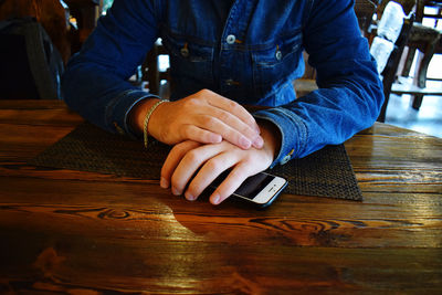 Midsection of man using mobile phone while sitting on table